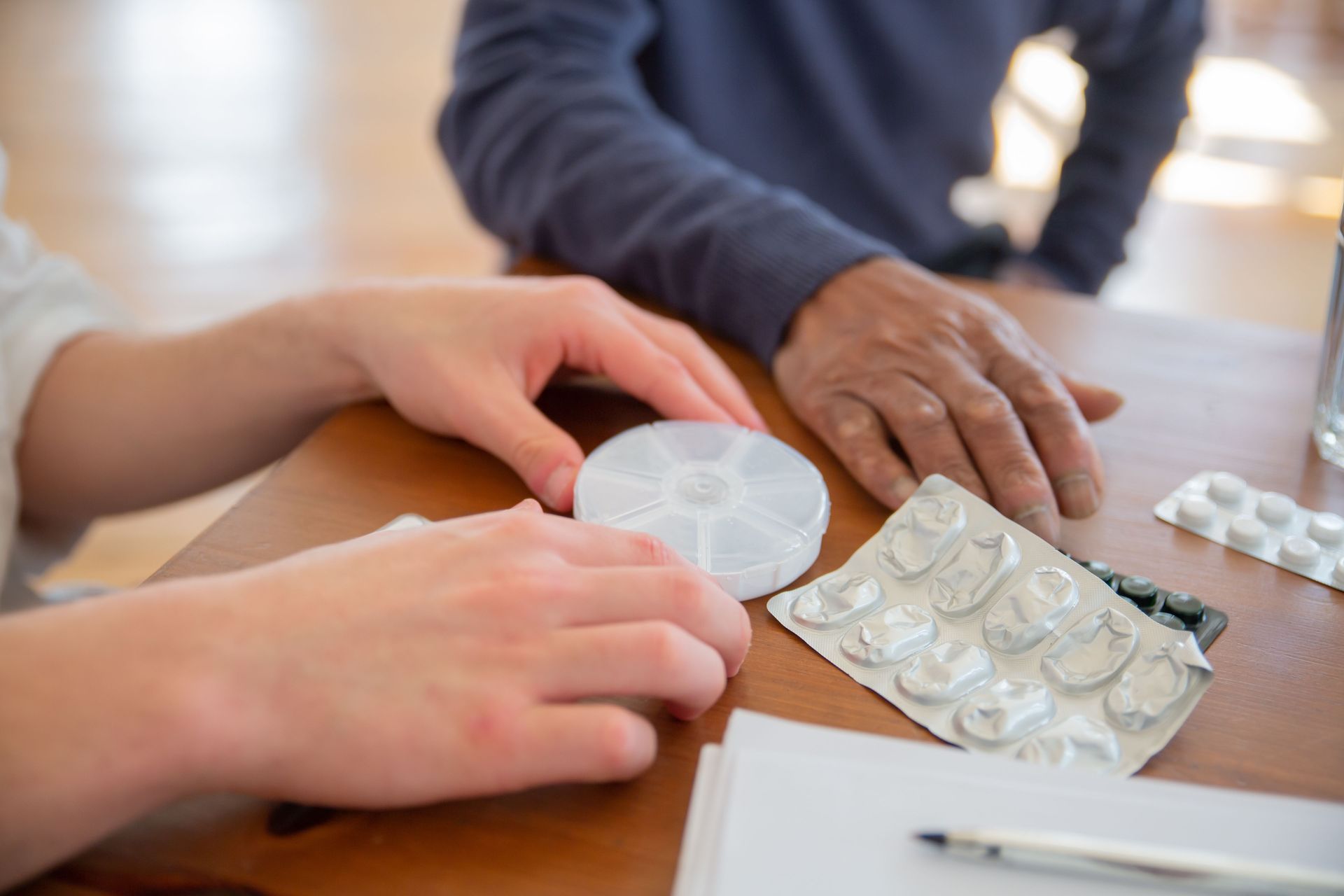 Close-up of hands sorting medicine and pill organizer on a wooden table.